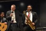 student with saxophone laughs while professor tells a story during a concert