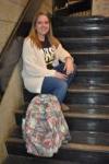 female student sitting on stairs with book bag in front of her
