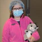 child wearing surgical mask and cap and holding stuffed animal
