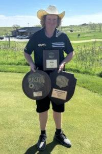 golfer on golf course holding two award plaques